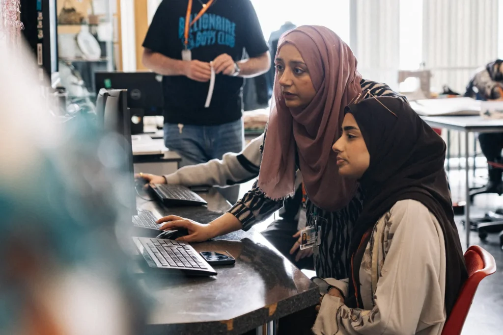 female muslim tutor and student in a computer lab on a computer sat at a desk