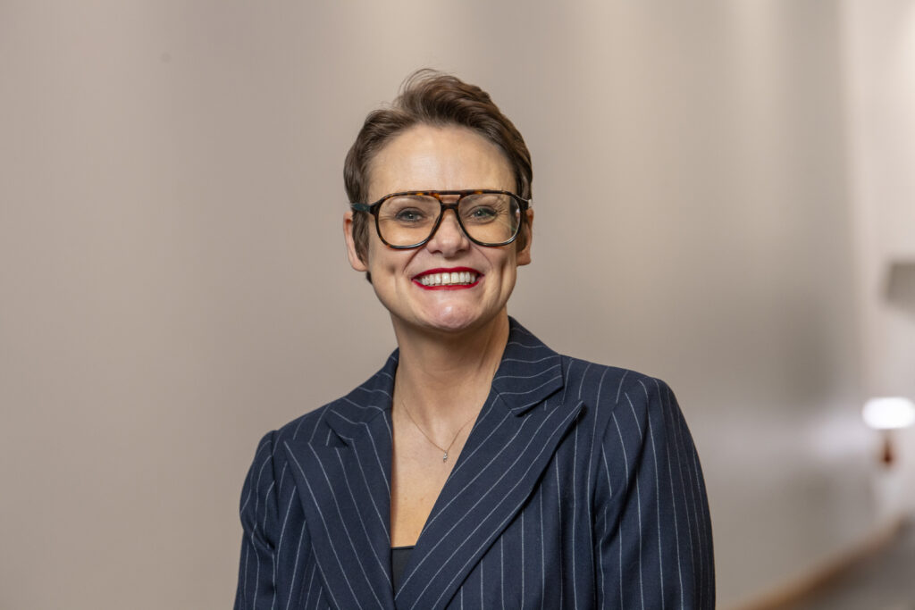 Image of Lisa O'Loughlin, Principal and CEO of East Lancashire Learning Group, smiling against a beige background. Lisa has short dark hair, glasses and is wearing a dark blue jacket.