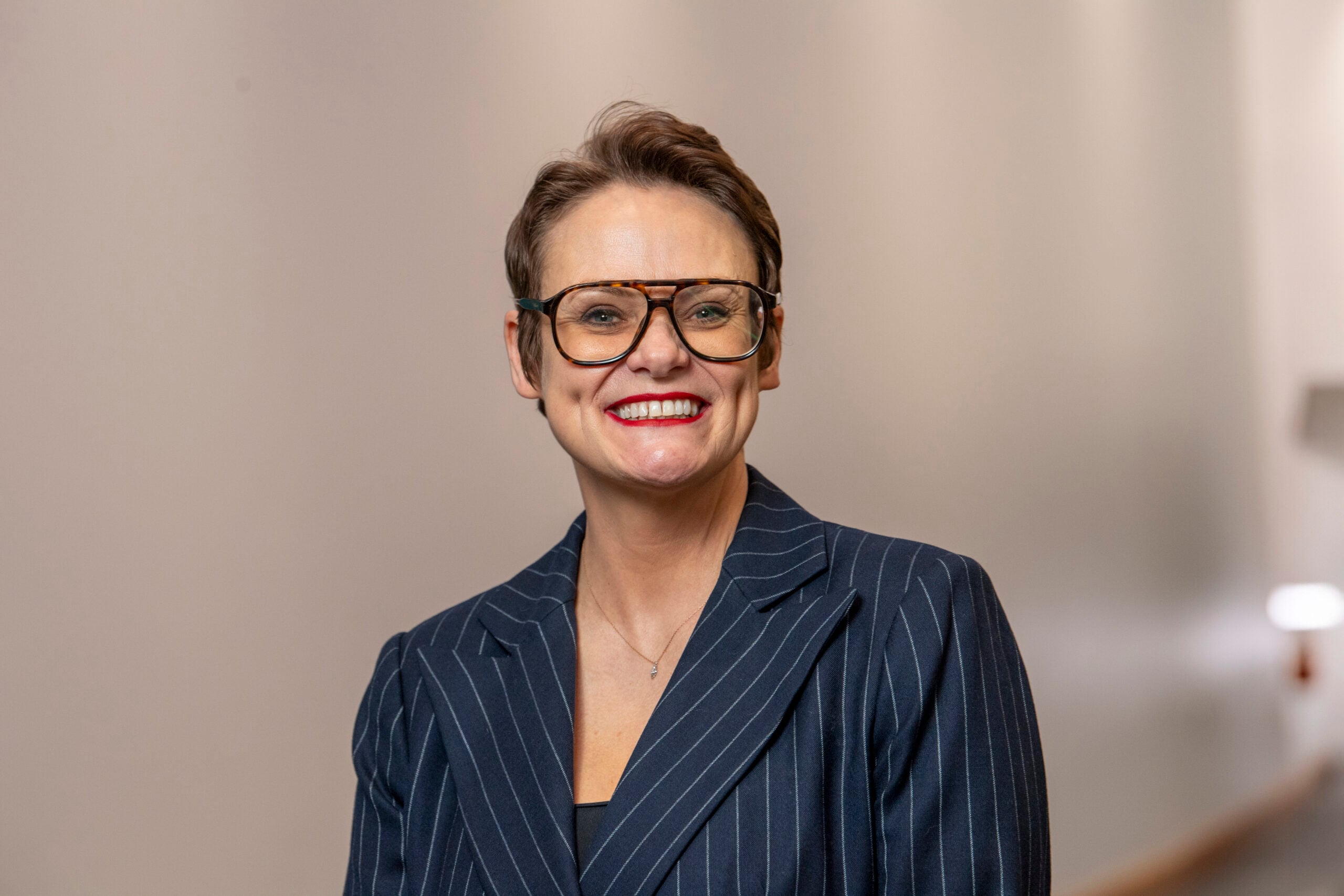 Image of Lisa O'Loughlin, Principal and CEO of East Lancashire Learning Group, smiling against a beige background. Lisa has short dark hair, glasses and is wearing a dark blue jacket.